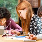 Young girls doing homework together at desk with tablets.